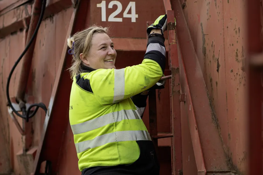 Kvinnlig anställd klättrar på container vid Svinryggens kretsloppsanläggning.